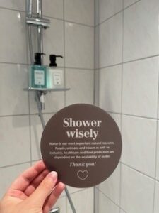 En hand som håller i en dekal med texten Shower Wisely.