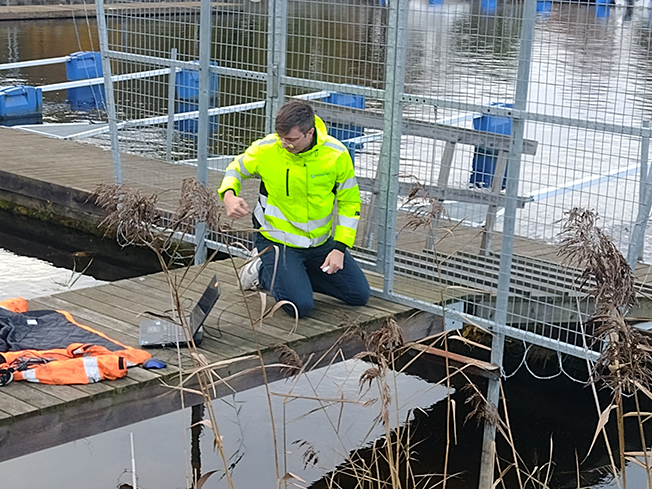 August Bjerkén sitter på en brygga för att placerar ut vattenståndsmätare.